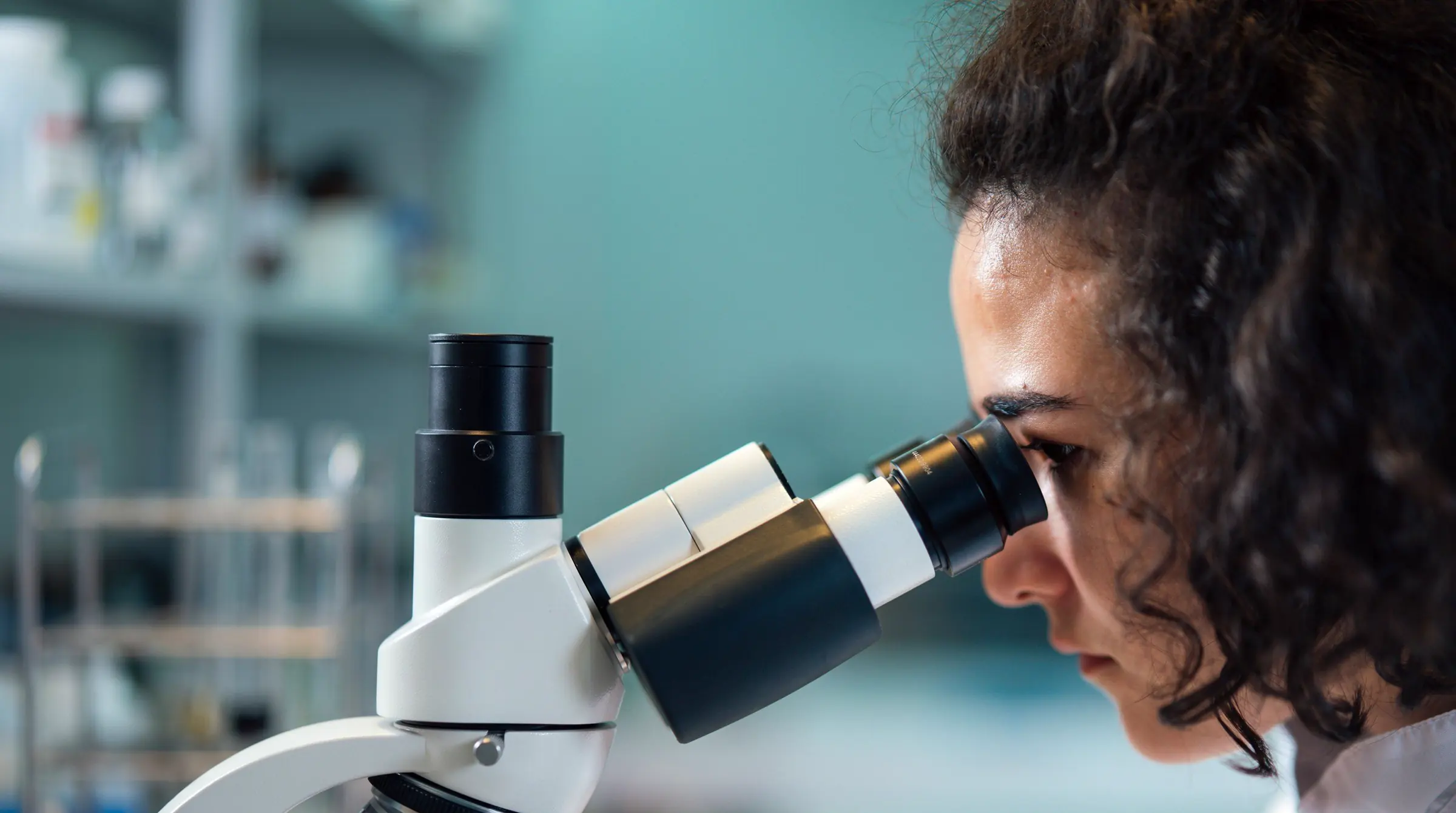 A scientist with curly hair looking into a microscope in a laboratory.