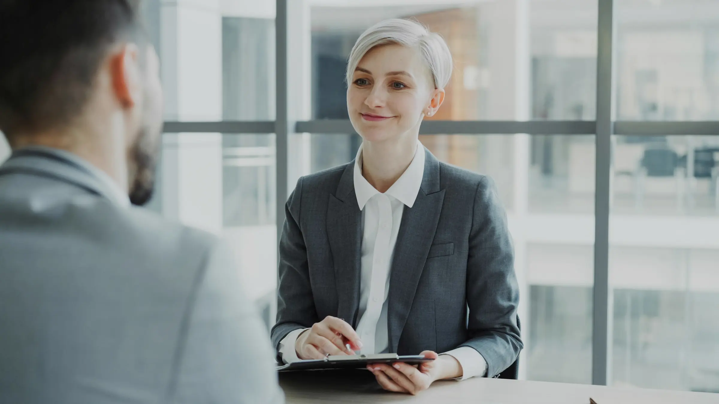 A recruiter in a grey blazer talks with a candidate across a table.